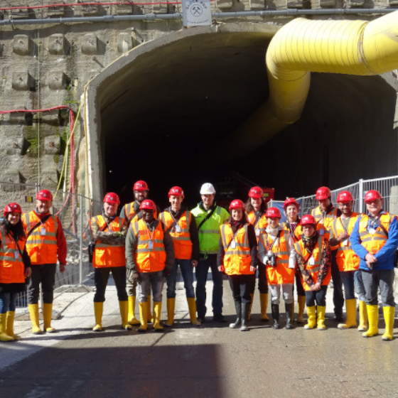 Gruppe von Besuchern in Sicherheitskleidung vor einem Tunnelportaleingang.